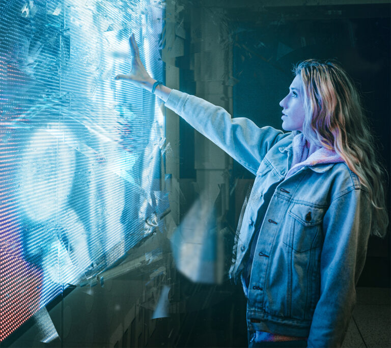 Photo of a young blonde woman reaching up towards an illuminated screen