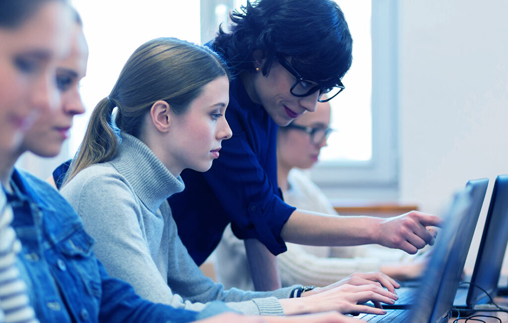 Woman teaching a younger woman tech skills on a laptop in a classroom