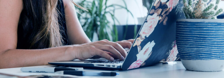 Young woman typing on a laptop with floral stickers on the back